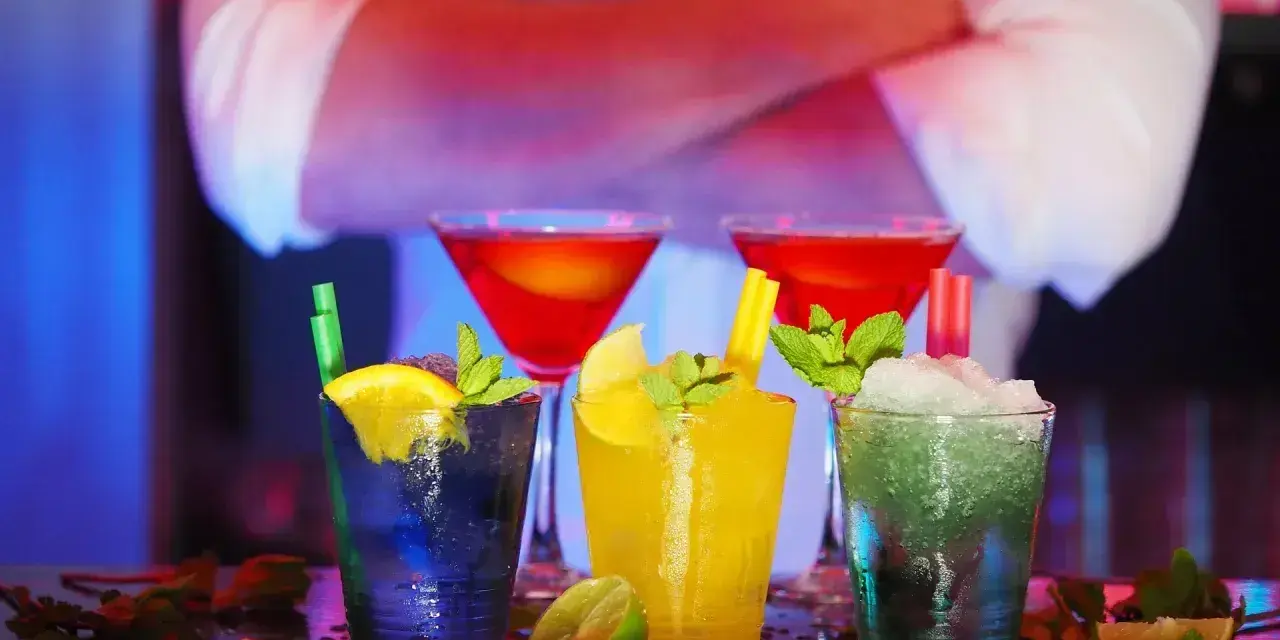 Kolorowe drinki na barze, a za nimi sylwetka barmana. Zastanawiasz się, ile zarabia barman na dyskotece?