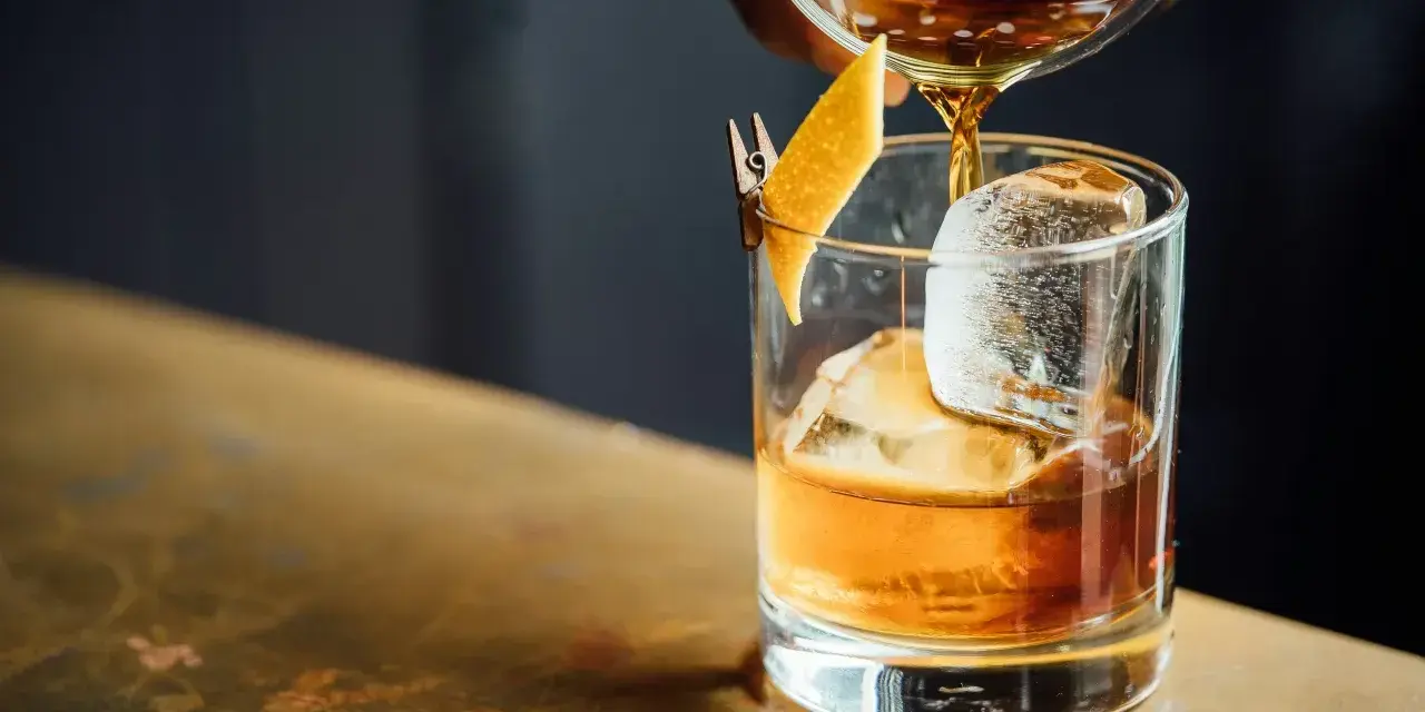 Idealny moment, by drink whisky z colą. Bursztynowy płyn z lodem i skórką pomarańczy.