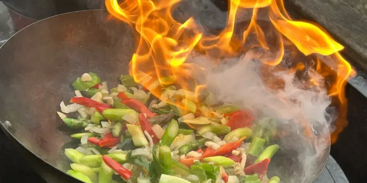 Pyszny stir-fry przepis w akcji! Warzywa w woku płoną żywym ogniem, tworząc apetyczny dym.