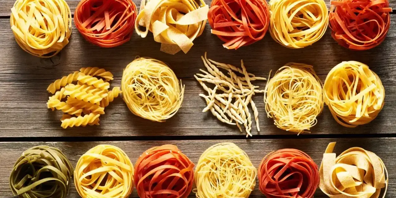Różne rodzaje makaronu, w tym porcja makaronu spaghetti, ułożone na drewnianym blacie.