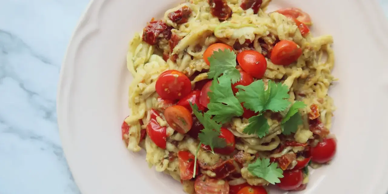 Pyszne dietetyczne spaghetti z cukinii z pomidorkami koktajlowymi i suszonymi pomidorami, udekorowane świeżą kolendrą.