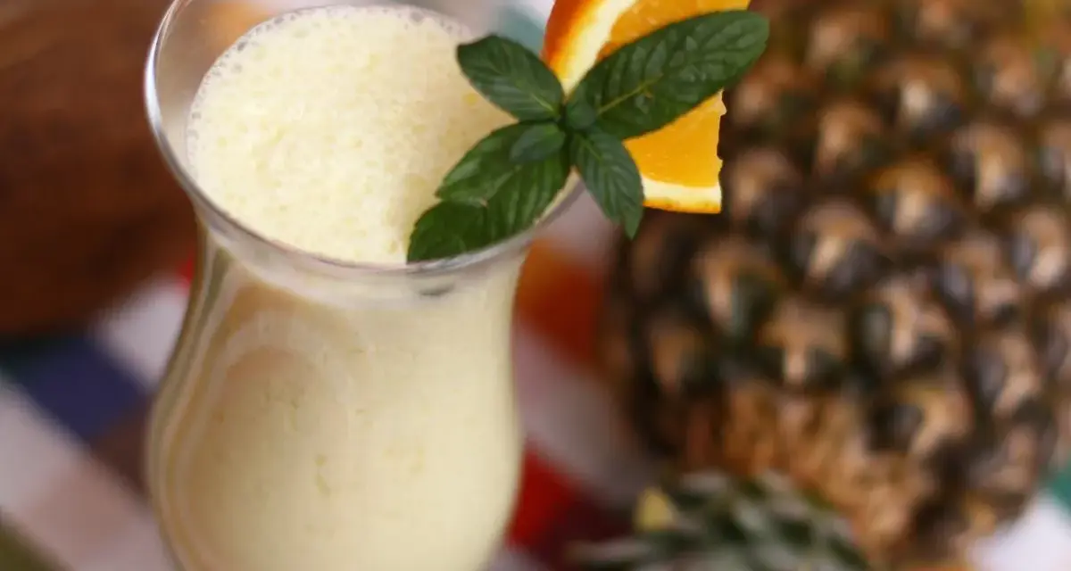 Orzeźwiający drink z ananasem, ozdobiony plasterkiem pomarańczy i miętą, na tle całego owocu.