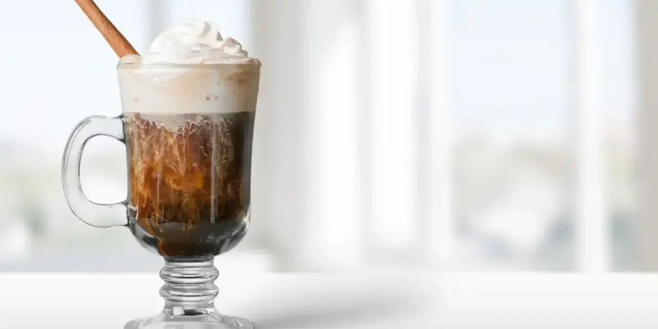 Pyszny irish coffee drink z bitą śmietaną i laską cynamonu, idealny na chłodny wieczór.