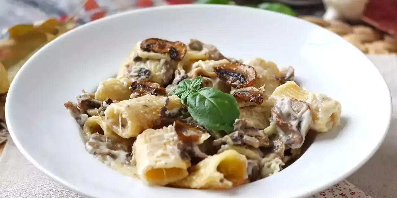 Pyszne spaghetti z grzybami w kremowym sosie, udekorowane listkiem bazylii. Idealne na jesienny obiad.