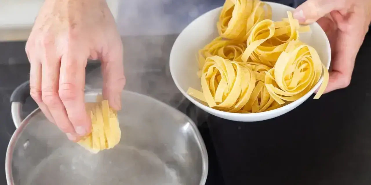 Ręka wkłada tagliatelle do wrzącej wody. Kluczowe jest, na jakim ogniu gotować makaron, by był al dente.