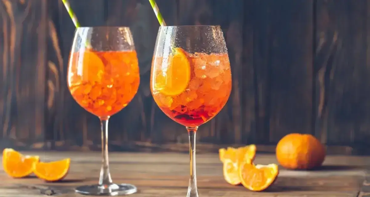 Dwa orzeźwiające drinki z aperolem, ozdobione plastrami pomarańczy i słomkami, na drewnianym blacie.