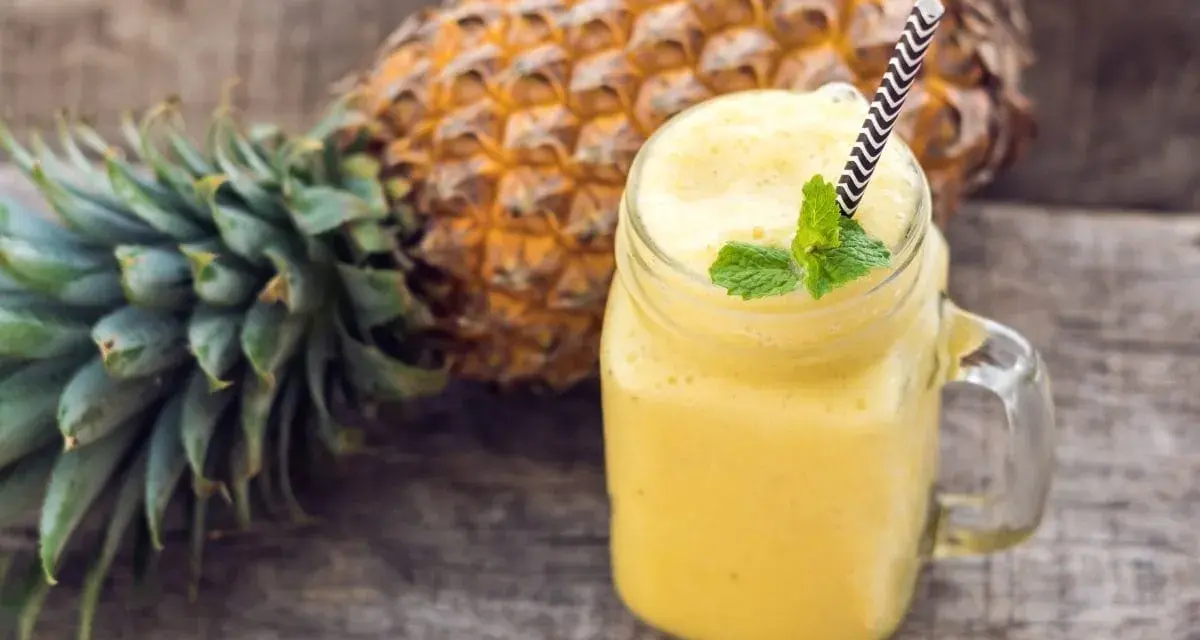 Orzeźwiający koktajl z ananasa i banana, ozdobiony miętą, na drewnianym tle.