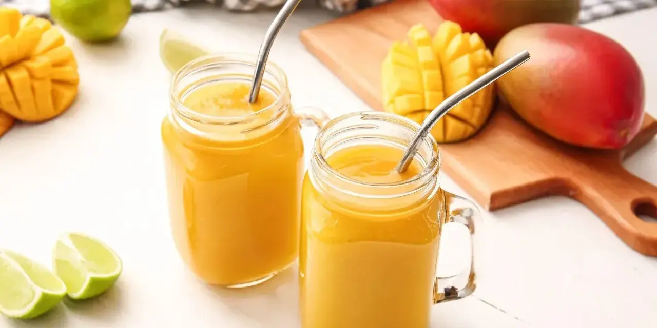 Orzeźwiający drink z wódką mango, podany w słoiczkach z metalowymi słomkami, obok świeżych owoców mango i limonek.