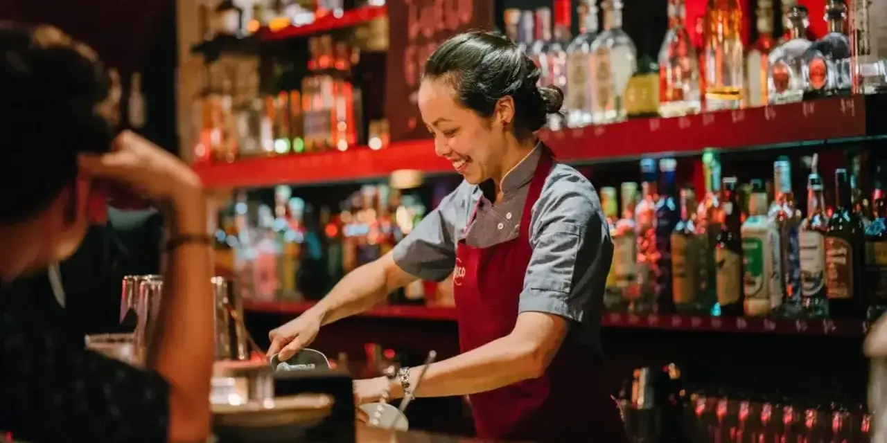 Uśmiechnięta barmanka przygotowuje drinki za ladą pełną alkoholi. Ciekawe, ile zarabia barman w Turcji?