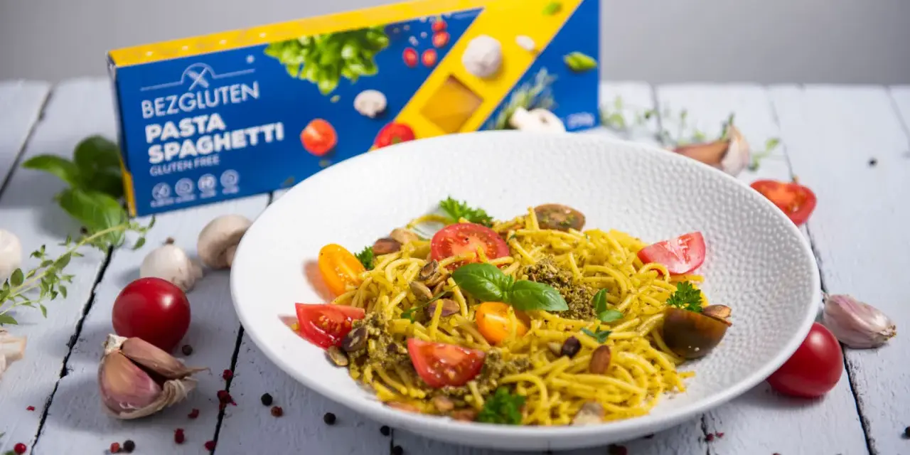 Pyszny talerz makaronu spaghetti bezglutenowego z pesto, pomidorkami i migdałami. Obok pudełko makaronu.