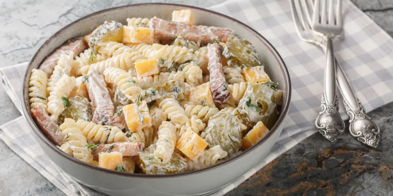 Sałatka z makaronem penne, szynką, serem i ogórkiem kiszonym, polana kremowym sosem.