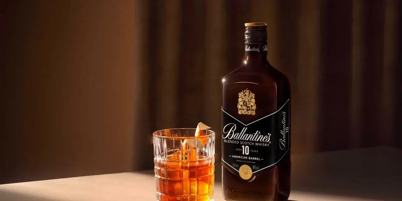 Whiskey z colą kontra Whiskey z ginger ale. Szklanka z bursztynowym trunkiem i butelka Ballantine's 10 Years Old.