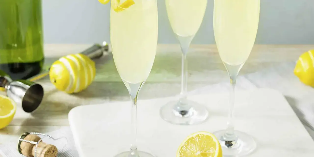 Trzy kieliszki musującego drinka French 75, jeden na ginie, drugi na koniaku, z cytrynową dekoracją.