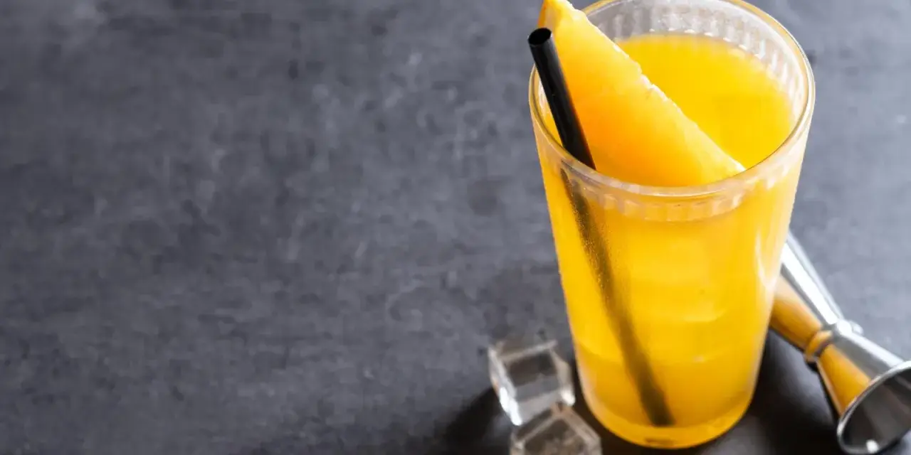 Orzeźwiający drink z wódką i sokiem pomarańczowym, ozdobiony plasterkiem pomarańczy, z kostkami lodu i miarką barmańską obok.