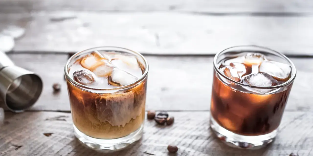 Dwa drinki na drewnianym blacie: jeden to White Russian, drugi to Black Russian.