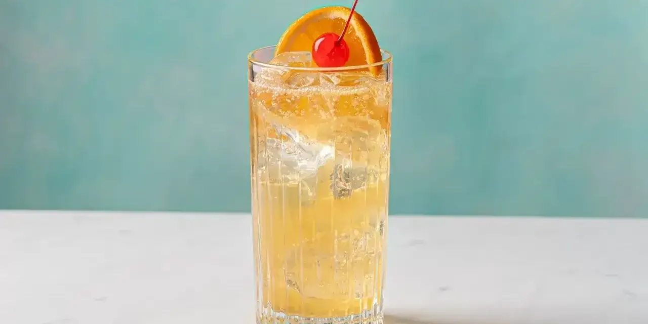 Orzeźwiający John Collins drink z lodem, plasterkiem pomarańczy i wisienką na tle turkusowej ściany.