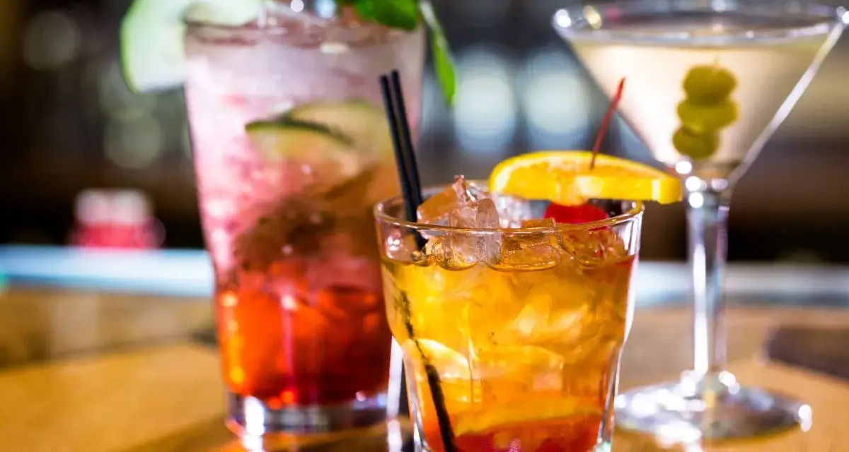 Kolorowe drinki z wódką smakową: czerwony z ogórkiem i miętą, bursztynowy z pomarańczą i wiśnią, oraz martini z oliwkami.