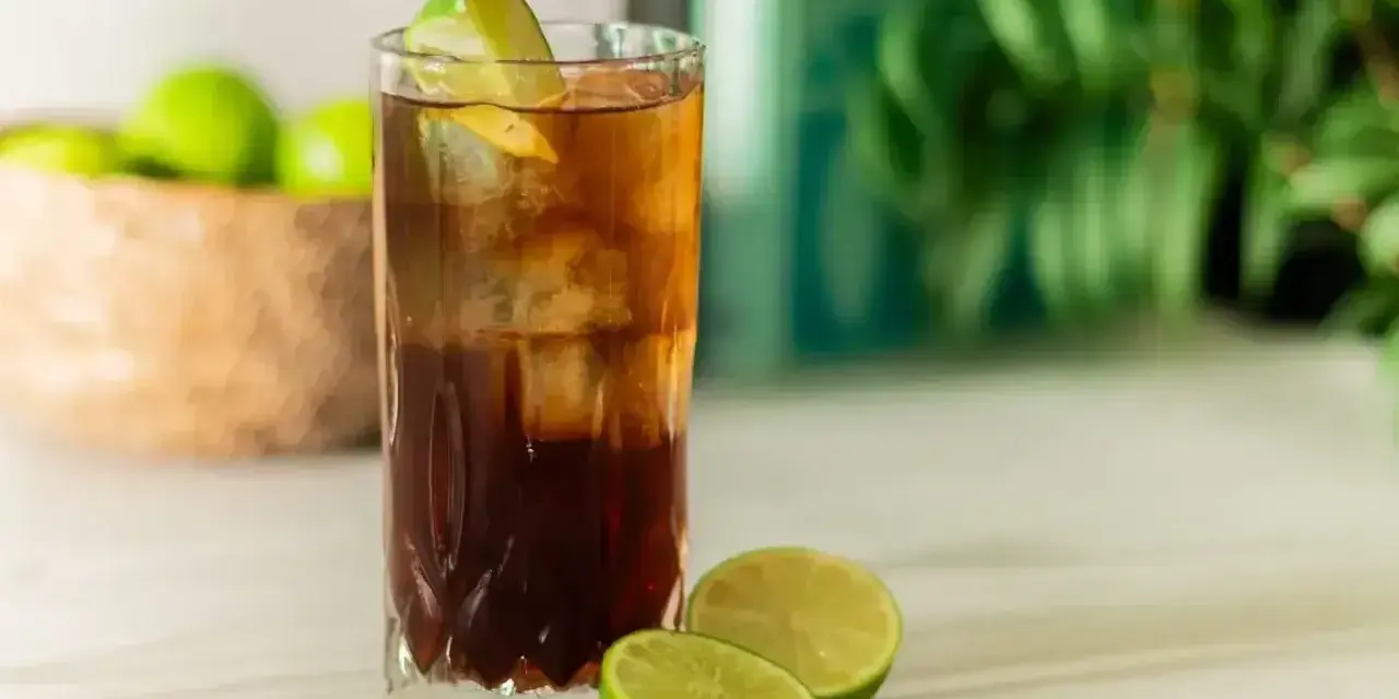 Orzeźwiający Cuba Libre, czyli rum z colą i limonką, z kostkami lodu i świeżymi limonkami w tle. Idealny na upalne dni.