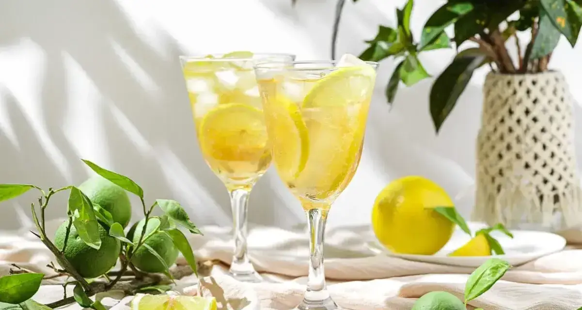 Orzeźwiający drink z cukrem na szklance, ozdobiony plasterkami cytryny i lodem. Obok świeże cytryny i limonki.