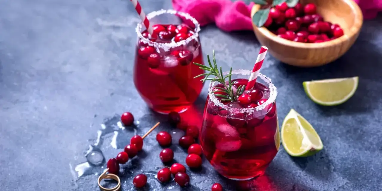 Dwa orzeźwiające drinki z grenadiną, ozdobione żurawiną i rozmarynem, z limonką w tle.