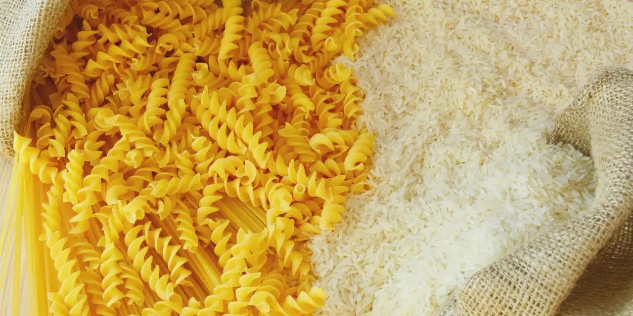 Ryż vs makaron: obok siebie leżą dwa rodzaje produktów. Z worka wysypano biały ryż, a obok niego spiralne fusilli i długie spaghetti.