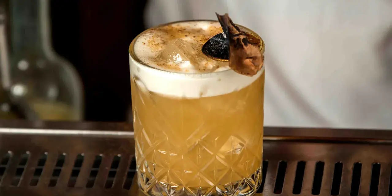 Elegancki Whisky Sour i Amaretto Sour z pianką i dekoracją na barze.