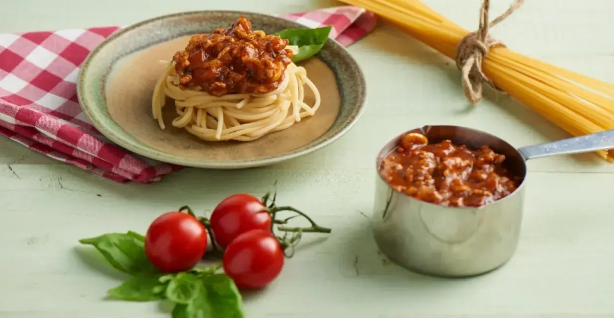 Pyszne spaghetti z sosem bolońskim, przygotowane z pomocą przyprawy do spaghetti Knorr. Obok świeże pomidory i bazylia.