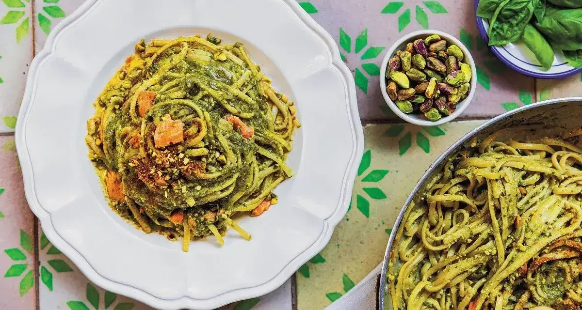 Pyszny makaron z zielonym pesto i pistacjami, wyglądający jak makaron jak z restauracji. Obok miseczka z pistacjami i listki bazylii.