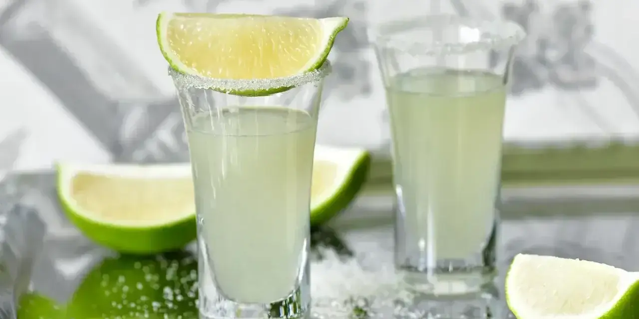 Wściekłe psy drink jak zrobić: dwa kieliszki z solą i limonką, obok ćwiartki limonki.