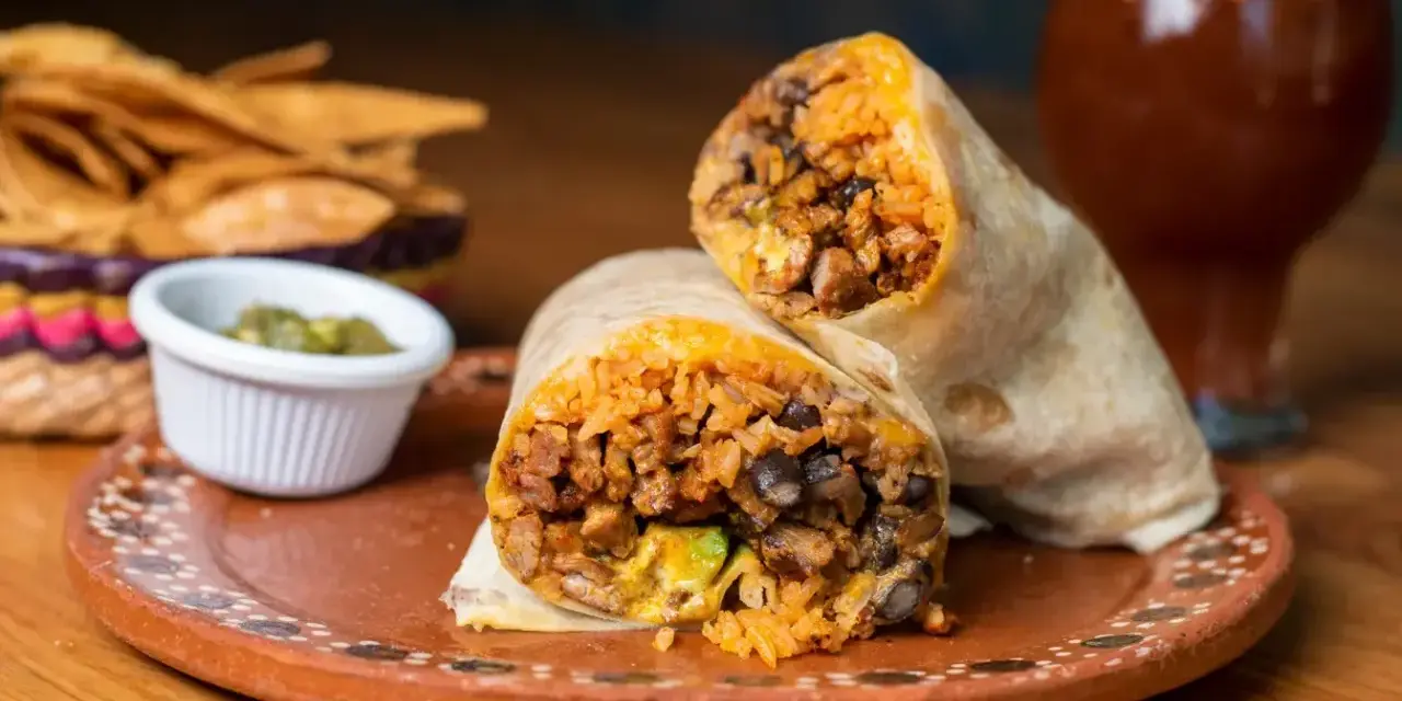 Pyszny burrito przepis: soczyste mięso, ryż, fasola i awokado zawinięte w tortillę. Obok chipsy i sos.