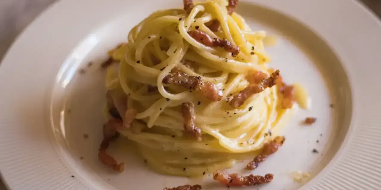 Pyszne spaghetti carbonara, idealne na prosty przepis. Kremowy sos, chrupiący boczek i czarny pieprz na talerzu.