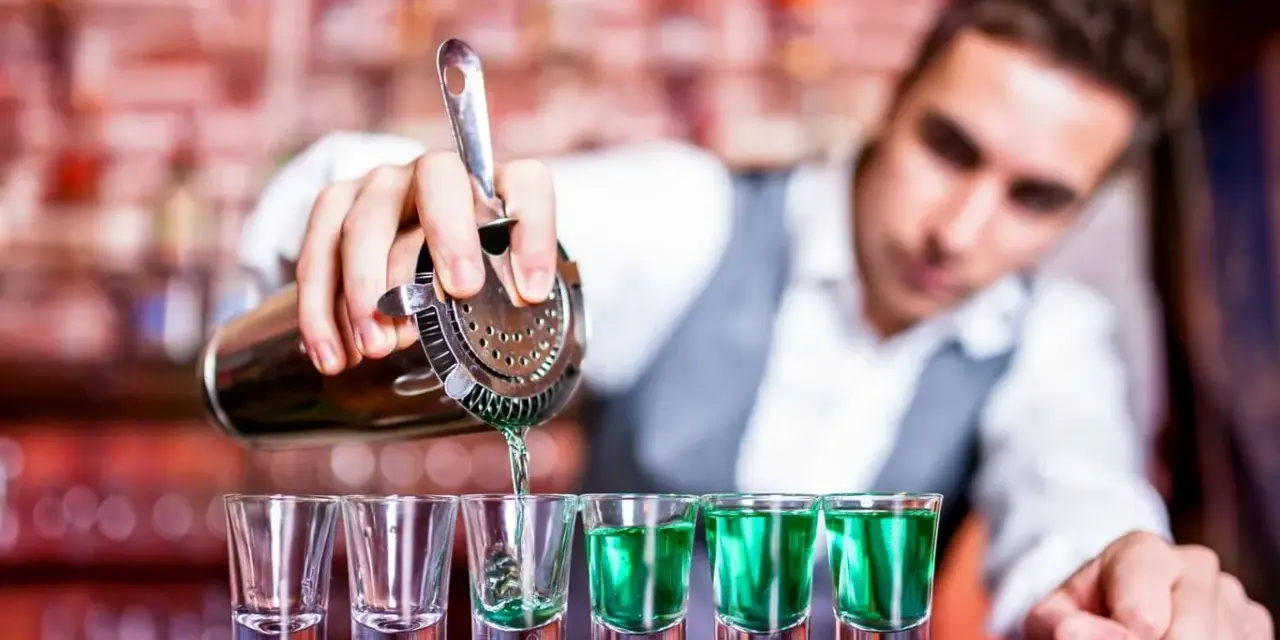 Barman nalewa zielony shot. Zastanawiasz się, ile kosztuje kurs barmana? To inwestycja w przyszłość!
