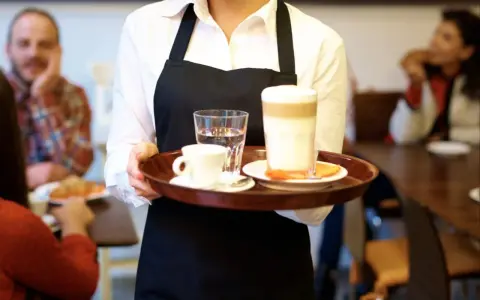 Kelnerka niesie tacę z kawą i wodą. Zastanawiasz się, ile zarabia barman w Sopocie?