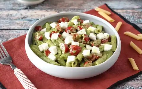 Makaron z pesto ze słoika przepis: penne z zielonym pesto, pomidorkami koktajlowymi i kostkami mozzarelli w białej misce.