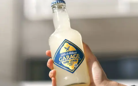 Ręka trzyma butelkę Seth & Riley's GARAGE Hard Lemon, orzeźwiający drink z piwem.