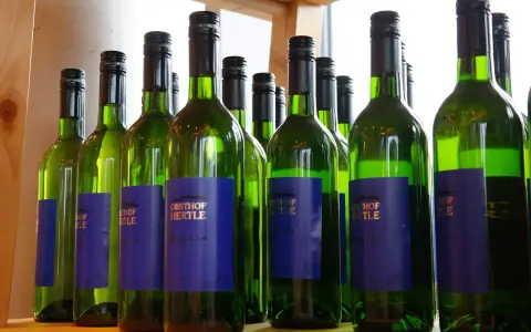 Rząd zielonych butelek białego wina Obsthof Hertle. Lepiej pić drinki czy białe wino? Wybór należy do Ciebie!