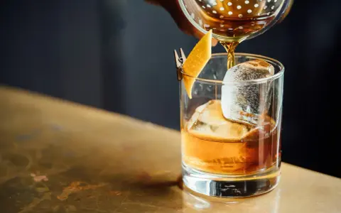 Idealny moment, by drink whisky z colą. Bursztynowy płyn z lodem i skórką pomarańczy.