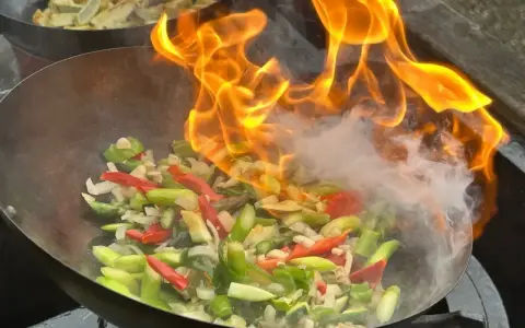 Pyszny stir-fry przepis w akcji! Warzywa w woku płoną żywym ogniem, tworząc apetyczny dym.