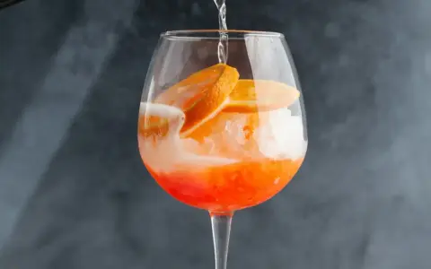 Orzeźwiający drink z cydrem, lodem i plasterkami pomarańczy, przygotowywany w dużym kieliszku.