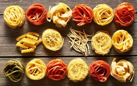 Różne rodzaje makaronu, w tym porcja makaronu spaghetti, ułożone na drewnianym blacie.