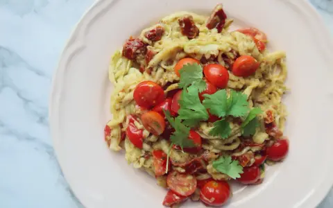 Pyszne dietetyczne spaghetti z cukinii z pomidorkami koktajlowymi i suszonymi pomidorami, udekorowane świeżą kolendrą.