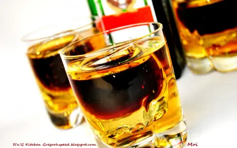 Dwa kieliszki z warstwowym drinkiem Jägermeister i Red Bull. Butelka Jägermeister w tle.