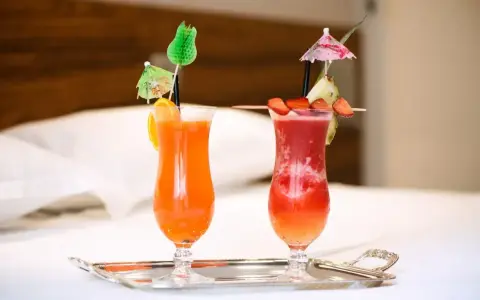 Dwa orzeźwiające drinki: jeden pomarańczowy z pomarańczą, drugi czerwony z truskawkami i ananasem, oba z parasolkami. Idealne na wakacje, może z dodatkiem triple sec.