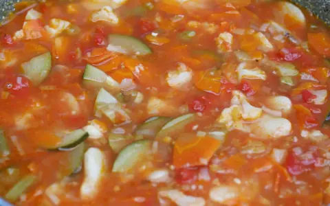 Gęsta, aromatyczna zupa jarzynowa, przypominająca włoskie minestrone, z kawałkami marchewki, cukinii i kalafiora w pomidorowym sosie.