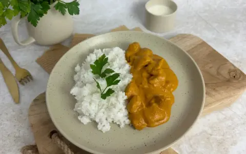 Pyszny Butter Chicken przepis na talerzu z ryżem i natką pietruszki. Idealny obiad.