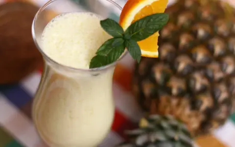 Orzeźwiający drink z ananasem, ozdobiony plasterkiem pomarańczy i miętą, na tle całego owocu.
