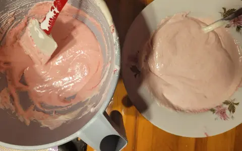 Różowa masa na makaroniki w misce i na talerzyku. Szpatułka miesza kremową konsystencję. Idealny makaroniki przepis w przygotowaniu.