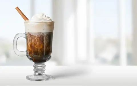 Pyszny irish coffee drink z bitą śmietaną i laską cynamonu, idealny na chłodny wieczór.