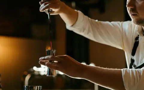 Barman nalewa ciemny płyn do jiggera, przygotowując drinka z Jägermeisterem i sokiem pomarańczowym.