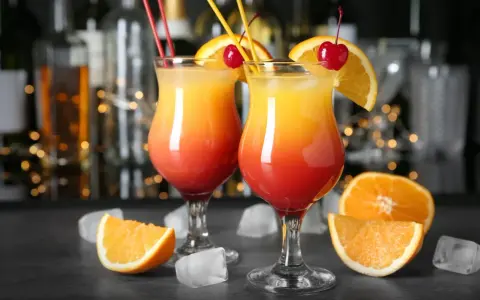 Dwa kolorowe drinki z parasolką, ozdobione pomarańczą i wiśnią, stoją na barze.